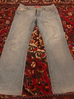 Ljusblå bootcut jeans  - Ljusblå jeans från Pepe Jeans med klassisk femficksmodell och bootcut passform. Jeansen har en röd logotyp på insidan av linningen och är tillverkade i bomull. Perfekta för en avslappnad och trendig look. Vintage!