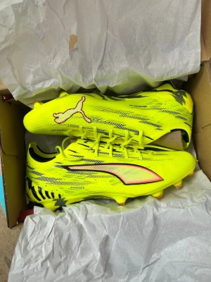  Puma fotbollsskor - Säljer ett par grymma neongula fotbollsskor från Puma med svarta och orange detaljer. Skorna har låg profil, snörning och mönstrad sula för bra grepp på planen. Tillverkade i syntetmaterial för lätt känsla och snabbhet. Perfekta för dig som vill sticka ut på planen.