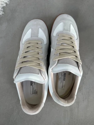  sneakers vita - Snygga  sneakers i vitt och ljusgrått med beigea skosnören. Ovandelen är i en mix av mocka och läder, klassisk låg modell med gummisula. Perfekta för dig som gillar minimalistisk och stilren design.