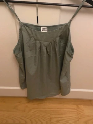 Grön topp - Snygg grön topp från Vero Moda med tunna axelband och avslappnad passform. Toppen har en enkel design med lätt rynk vid halsringningen och är perfekt för varma dagar.