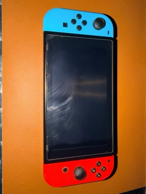 Nintendo Switch konsol med tillbehör  - Nintendo Switch spelkonsol med en blå Joy-Con på vänster sida och en röd Joy-Con på höger sida. Konsolen har en stor skärm i mitten och är tillverkad i plast. Perfekt för gaming på språng eller hemma. Tre spel medföljer: Super Smash Bros Ultimate, Mario & Sonic at the Olympic Games och Luigi's Mansion 3. Två racing wheel kontroller och en pro controller med en liten och en stor väska för konsolen. Pris går att diskuteras 