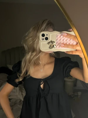 Svart blus med puffärm och knyt - Säljer en svart blus med puffärmar och söt knytning framtill. Blusen har en lätt v-ringad urringning och är tillverkad i ett mjukt, något strukturerat tyg. Perfekt för dig som gillar en feminin och trendig look.