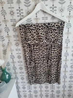 Leopardmönstrad axelbandslös klänning - Säljer en snygg axelbandslös klänning med leopardmönster. Klänningen är kort och har en beige bas med svarta och bruna fläckar. Perfekt för dig som vill sticka ut och gillar djurmönster. Materialet känns mjukt och följsamt.