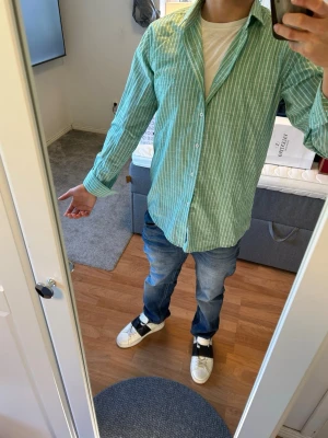 Polo Ralph Lauren skjorta  - Snygg grön skjorta med vita ränder, klassisk krage och knappar hela vägen. Tillverkad i lätt bomullsmaterial, perfekt för en avslappnad och fräsch stil. Långärmad modell som kan bäras öppen eller stängd över t-shirt.