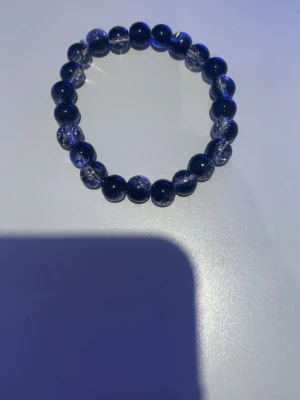 Blått pärlarmband med glaseffekt - Snyggt armband med runda, blå pärlor som har en glaseffekt och inslag av transparenta detaljer. Pärlorna är trädda på en elastisk tråd vilket gör det enkelt att ta på och av. Perfekt accessoar för att addera lite färg till din stil.