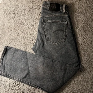 Grå jeans från G-Star RAW - Säljer ett par kall blåa jeans från G-Star RAW med raka ben. Jeansen har en diskret tvättad look och svart patch med logga bak i midjan. Storlek W28 L30. Endast använda ett fåtal gånger!