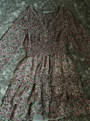 Klänning från Zara - Supersöt volangklänning från Zara med rosa och grönt blommönster. Klänningen har långa ärmar, smock i midjan, volangdetaljer och guldiga knappar framtill. Tyvärr är den för liten för mig just nu men har varit perfekt för sommarens alla tillfällen!