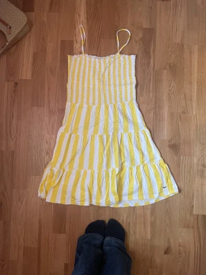 Gul och vit randig sommarklänning - Säljer denna söta gul och vit randiga klänningen med smala axelband och volanger. Klänningen har en smockad överdel, perfekt för varma sommar dagar. Endast provad på! Skriv om ni har frågor och priset går att diskutera❤️