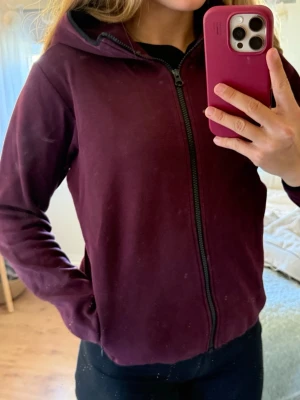 Vinröd hoodie med dragkedja - Säljer en vinröd hoodie med dragkedja framtill och huva. Hoodien har långa ärmar och är tillverkad i ett mjukt, bekvämt material. Perfekt för chill dagar eller när du vill ha något enkelt men snyggt.