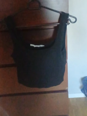 Svart cropped linne med breda axelband - Snyggt svart cropped linne med breda axelband och fyrkantig ringning. Perfekt att styla till jeans eller kjol för en trendig look. Mjuk och stretchig bomullsblandning som sitter skönt på kroppen.