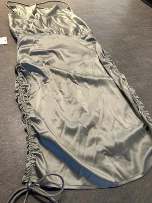 Bubbleroom helt ny dusty green satin öppen rygg klänning - Helt ny klänning från Bubbleroom i storlek 36, fortfarande med lapp kvar. Satinliknande modell i “dusty green” med öppen rygg och knytning bak, vilket ger en väldigt fin och feminin look. Draperad framtill och justerbara snören på sidorna så man kan anpassa passformen. Superfin på, men tyvärr har fått stå i garderoben.