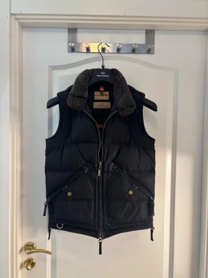 Parajumpers väst Masterpiece Series (utgången modell) + galge – XS - Säljer en Parajumpers väst från den populära Masterpiece Series – en modell som inte längre tillverkas.  Storlek XS (slim fit) i svart färg. Västen är äkta och har QR-kod för verifiering.  Detaljer: • Utgången modell (produceras inte längre) • Masterpiece Series • Färg: Svart • Storlek: XS (slim fit) • Pälsfodrad krage • Flera fickor och klassiska PJS-detaljer • Original Parajumpers-galge medföljer  Kan skickas eller mötas upp