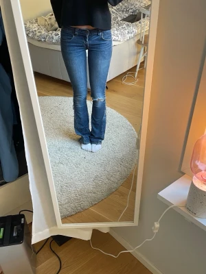 Levi’s bootcut bootcut jeans med slitning - Säljer ett par blå bootcut jeans med slitning vid knät. Jeansen har klassisk femficksdesign, normal midja och är tillverkade i denim med lätt stretch. Perfekta för en avslappnad och trendig look.