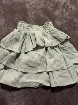 Ljusgrön volangkjol med resårmidja - Supersöt ljusgrön kortkjol med flera volanger och bred resår i midjan. Kjolen har en luftig känsla och passar perfekt till varma dagar. Enkel att matcha med både toppar och sneakers för en chill look.