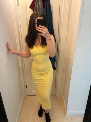 Gul ribbad långklänning - Säljer en snygg gul långklänning med smala axelband och ribbad struktur. Klänningen har en figurnära passform och slits bak för extra rörelsefrihet. Perfekt för sommarens alla tillfällen!