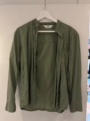 Grön henley-skjorta från H&M - Snygg grön henley-skjorta från H&M i mjuk bomull. Skjortan har lång ärm, knappar framtill och en avslappnad passform. Perfekt för dig som gillar enkel och stilren design.