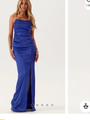 Blå långklänning med snörning - Snygg blå långklänning med slits framtill och smickrande drapering. Klänningen har smala axelband, öppen rygg med snörning och är tillverkad i ett glansigt material som ger en lyxig känsla. Passar till en bal eller en finare tillställning, använts en gång!😇😇💕