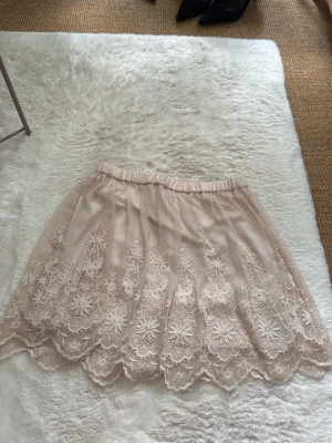 Beige kjol med spets och broderi - Söt beige kortkjol med vacker spets och broderade blommönster. Kjolen har elastisk midja och är super skön, från h&m (divided) i storlek 36 (s)