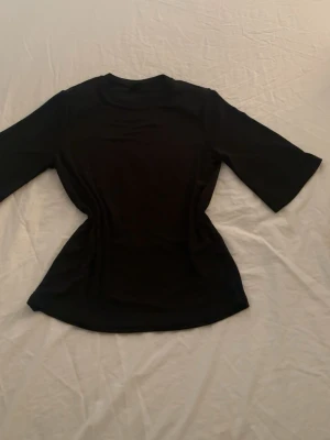 Svart topp från Gina Tricot - En svart, figurnära topp från Gina Tricot med rund halsringning och halvlånga ärmar. Enkel och stilren design som passar till många olika looks. Tillverkad i mjukt material som känns skönt mot huden.