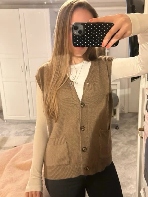 Brun stickad väst med knappar - Mysig brun stickad väst med v-ringning och knäppning framtill. Västen har två fickor fram och ribbade kanter. Köpt på plick utan lapp, passar storlek S/M!! Inga skador!!💘💘💘