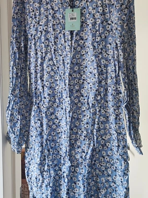 Helt ny Morris Stockholm klänning  - Supersöt blå klänning med vitt och svart blommönster. Långärmad modell med avslappnad passform och v-ringning. Perfekt för vår och sommar, tillverkad i ett lätt och luftigt material. Märke: Morris. Material: Kupro och viskos