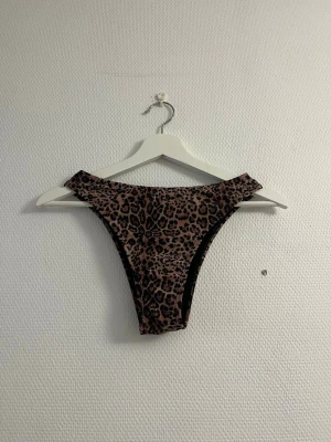 Leopardmönstrad bikiniunderdel - Säljer en snygg bikiniunderdel med leopardmönster i bruna och svarta toner. Modellen har hög midja och skär upp över höfterna för en trendig look. Perfekt för dig som vill sticka ut på stranden eller vid poolen.