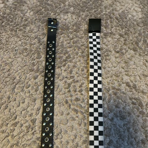 Två coola bälten, svart och rutigt - Säljer två bälten: ett svart bälte med silverfärgade nitar och hål, samt ett svartvitt rutigt bälte med plastspänne. Perfekta accessoarer för att lyfta din outfit.