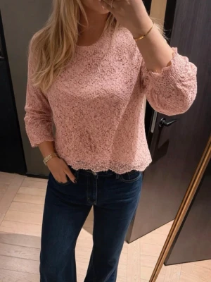 Rosa spetsblus  - Söt rosa blus i spets och rund halsringning. Blusen har fina volangdetaljer vid ärmslut och nederkant samt ett litet knappslå bak i nacken. Perfekt för dig som gillar romantisk och feminin stil.