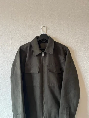Mörkgrön overshirt - Mörkgrön imitations mocka jacka från NEXT i storlek M sjukt trevlig till vår/ sommar. Skriv om ni vill ha bilder hur den sitter
