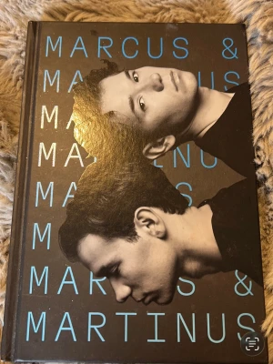 Marcus & Martinus bok med svart omslag - En snygg bok om Marcus & Martinus med hård pärm i svart och blått. Omslaget har porträtt av tvillingarna och deras namn tryckt i stora blå bokstäver. Perfekt för dig som gillar musik och vill veta mer om deras liv och karriär.
