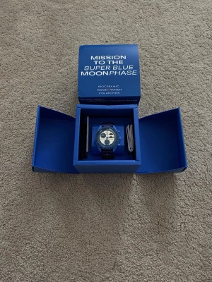 Swatch x Omega Super Blue Moonphase - Säljer en Swatch x Omega Mission to the Super Blue Moonphase från Bioceramic MoonSwatch Collection. Klockan har en blå boett och blått armband, med vit urtavla och blå detaljer. Snygg och unik design med månfaskomplication. Kommer i originalbox.