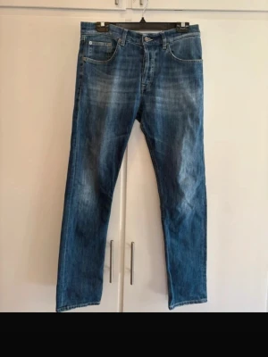 Blå dondup jeans med tvättad look - Säljer ett par klassiska blå jeans dundup med snyggt tvättad effekt framtill. Jeansen har fem fickor och normal midja. Perfekta till vardagsstilen och passar till det mesta. Materialet är denim i bomull.
