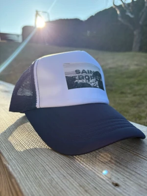 (Märke: LTHwear)Saint Tropez truckerkeps i blått och vitt - (PRIS: 249kr kan gå ner som mest till 239) Cool truckerkeps från Saint Tropez med vit frontpanel och blå skärm samt mesh på sidorna. Tryck med landskapsmotiv och text på framsidan. Perfekt för dig som vill ha en avslappnad och trendig look.