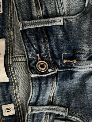 Blå slitna jeans från replay - Säljer ett par blå jeans med slitningar och hål på benen. Jeansen har en tvättad look och flera distressed detaljer som ger en cool och avslappnad stil. Perfekta för dig som gillar streetwear och vill ha ett par jeans med attityd.