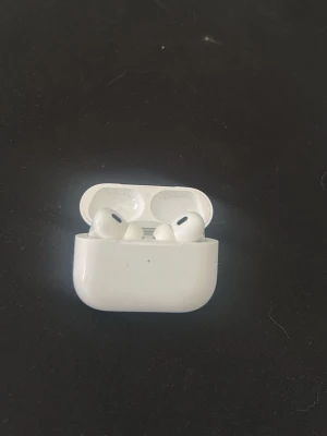 Apple AirPods Pro med laddningsetui - Säljer ett par vita Apple AirPods Pro. Hörlurarna har en stilren och kompakt design med silikonproppar för bra passform. Perfekta för musik, poddar och samtal. Laddningsetuiet har en LED-indikator på framsidan.
