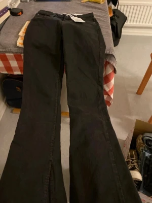 Svarta bootcut jeans med rå kant - Säljer ett par svarta bootcut jeans med rå, fransig kant längst ner. Jeansen har klassisk femficksdesign och är tillverkade i denim. Perfekta för dig som gillar en avslappnad och trendig look med lite edge.