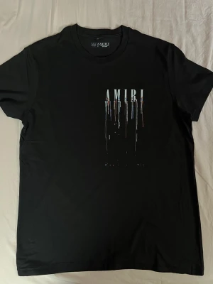 Svart t-shirt från Amiri med tryck - Cool svart t-shirt från Amiri med unikt tryck framtill och en stor silverfärgad ros med logotyp på ryggen. T-shirten har rund hals och korta ärmar, perfekt för dig som vill sticka ut med stil. Materialet är mjuk bomull och passformen är normal.