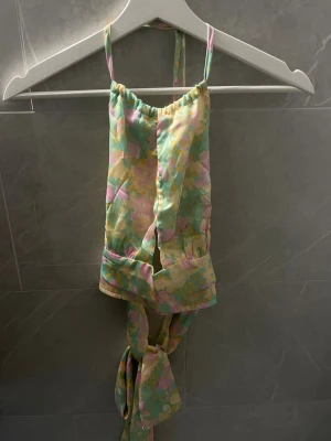 Pastellfärgad blommig topp - Söt topp i pastelliga färger med blommigt mönster. Modellen har smala axelband och knyt i ryggen för justerbar passform. Materialet känns mjukt och lätt. 