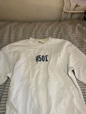 Vit sweatshirt från Levi's 501 - Säljer en vit sweatshirt från Levi's med blå 501-tryck på bröstet. Tröjan har relaxed fit, rund halsringning och långa ärmar. Perfekt för dig som gillar klassisk streetwear och enkel stil.