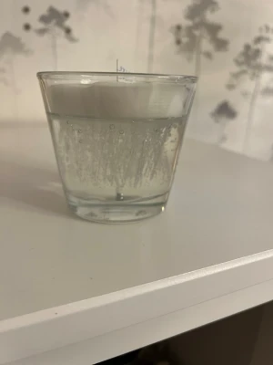 Isberget Doftljus Arctic Glow i glas - Säljer ett doftljus från GR med doften Arctic Glow. Ljuset är vitt och genomskinligt, gjutet i ett stilrent glas med etikett i blått och vitt. Perfekt för att skapa mysig stämning hemma.
