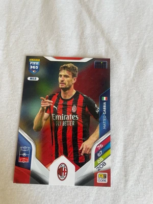 Panini FIFA 365 Adrenalyn XL samlarkort - Säljer ett Panini FIFA 365 Adrenalyn XL samlarkort med AC Milan-tema. Kortet har svart och röd design med spelare i matchtröja, samt statistik och klubbmärke. Baksidan har en aktiveringskod för online-spel. Perfekt för samlare av fotbollskort.
