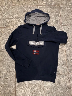 Mörkblå hoodie från Napapijri - Säljer denna feta napapijri hoodien!!👏🔥 Den är i riktigt fint skick och har en unik design samt en väldigt unik gömd ficka. Tröjan är i storlek S. Hör av er vid frågor👏🙌