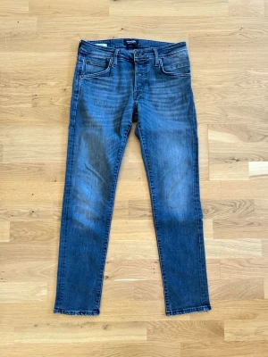 Svart slim fit jeans från Jack and Jones  - Säljer ett par klassiska blå slim fit jeans från jack&jones  Jeans. Jeansen har fem fickor, normal midja och smal passform hela vägen ner. Materialet är mjukt denim med lätt tvättade detaljer och kontrastsömmar. Perfekta för en avslappnad och stilren look.