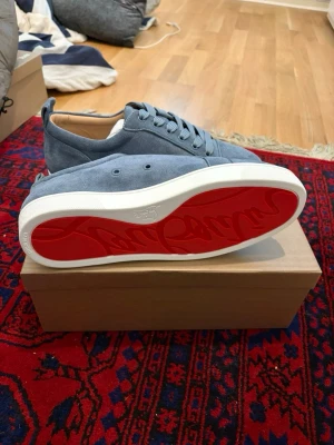 Blåa sneakers från Christian Louboutin - Snygga blåa sneakers i mocka från Christian Louboutin med klassisk röd sula och vita kanter. Skorna har rund tå, matchande blå skosnören och diskret design som känns både lyxig och stilren.