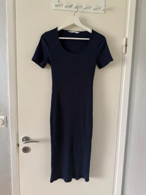 Långklänning - Snygg marinblå långklänning med ribbad struktur och korta ärmar. Klänningen har en rund halsringning och är figurnära i modellen, perfekt för en stilren look. Passar till många olika tillfällen och är enkel att styla med accessoarer.