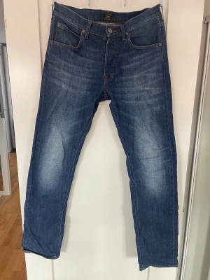 Blå raka/slim jeans från Lee - Säljer ett par klassiska blå jeans från Lee med rak/slim passform och snygga fades på låren. Jeansen har fem fickor, och är tillverkade i denim. Perfekta för en avslappnad och trendig look.