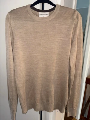 Brunn & Stengade Beige stickad tröja - 50% merinoull 50% Acrylic. Klassisk beige stickad tröja från Brunn & Stengade med rund halsringning och diskret broderad logga på bröstet. Tröjan har lång ärm och ribbade muddar vid ärmslut och nederkant. Perfekt för en stilren och enkel look. Fri frakt 🚚🤩⭐️ Inga defekter eller hål 📸