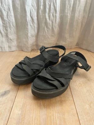 Svarta platåsandaler med remmar, helt i skinn, från Timbeland.  - Fina svarta sandaler med platåsula och flera korsade remmar över foten. Justerbart spänne vid ankeln för perfekt passform. Tillverkade i mjukt skinn med robust gummisula. Knappt använda! Perfekta för en trendig och avslappnad look.