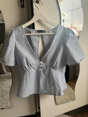 Blårandig topp med puffärm från SHEIN - Oanvänd. Snygg blårandig topp från SHEIN med djup v-ringning, puffärmar och knappar framtill. Tunt och lätt material, perfekt för sommaren.
