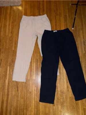 Beiga linnebyxor med dragsko - Snygga och luftiga beiga linnebyxor med resår och dragsko i midjan. Byxorna har raka ben och sidfickor, perfekta för en avslappnad stil. Tillverkade i linne för en skön känsla och bra andningsförmåga.